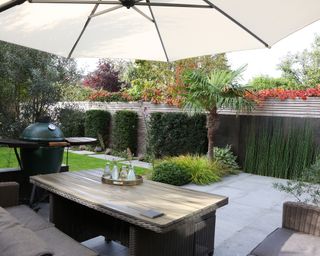A parasol over an outdoor seating area with geometric hedging