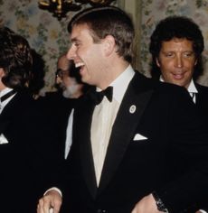 Prince Andrew in a tuxedo, laughing with Tom Jones standing behind him 
