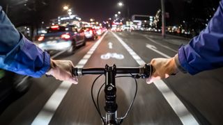 Image of man cycling down dark city street with lights