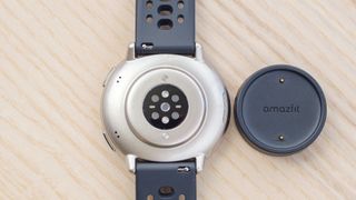 Close-up of the back of the Amazfit Active 2 smartwatch next to a small round charging puck