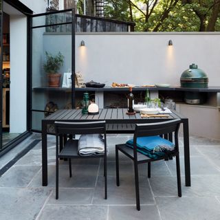 outdoor kitchen with open shelving, Big Green Egg, wall lights, grey worktop, black table and chairs