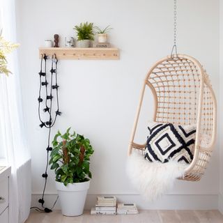 white wall with wooden shelf plant in white pot swinging chair with cushion