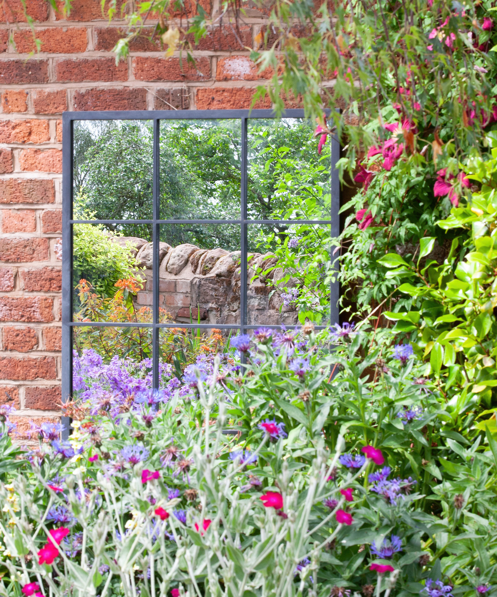 An outdoor mirror mounted on a red brick garden wall