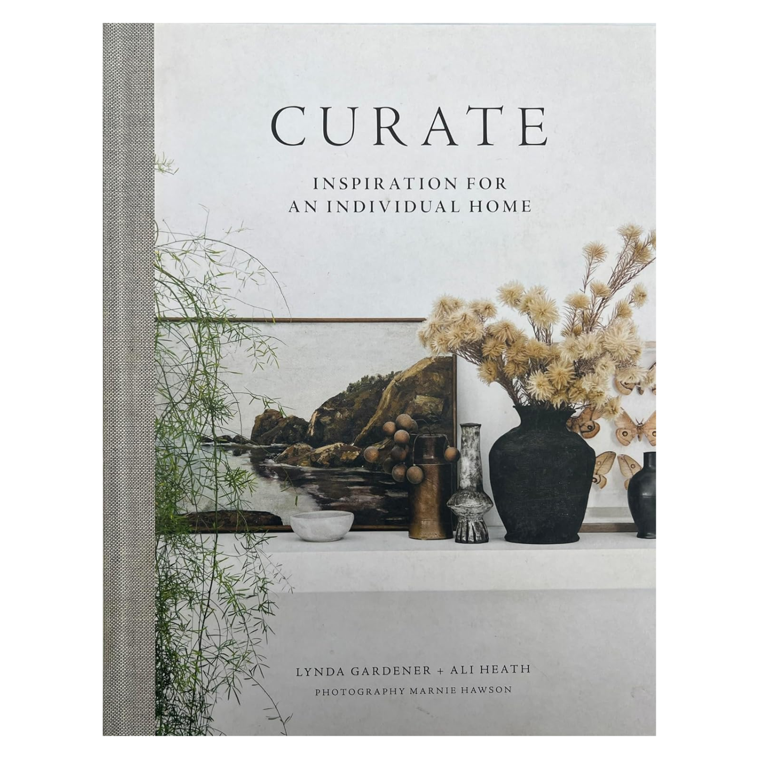 A hardcover book with a gray spine and a cover featuring a shelf of art, vases and decor