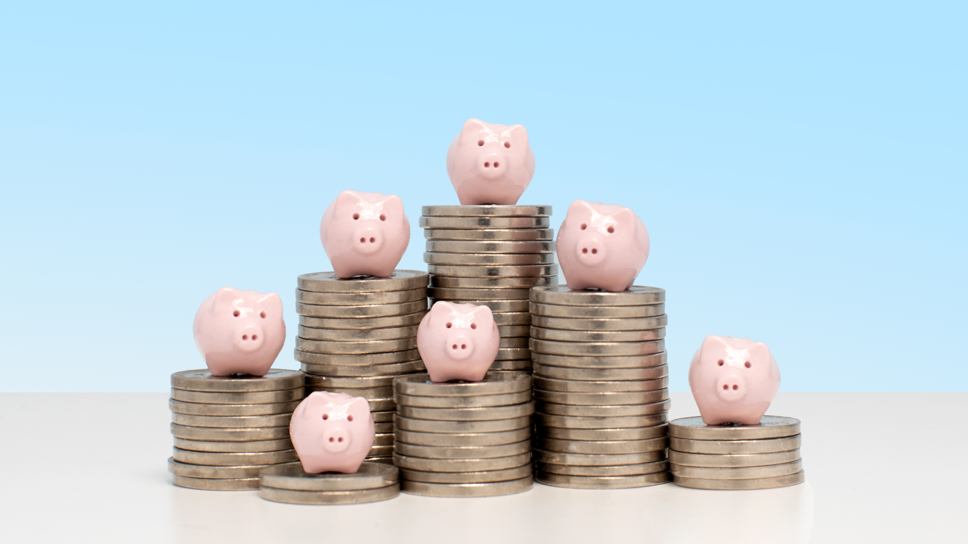Seven piggy banks sit on seven stacks of coins of varying heights.