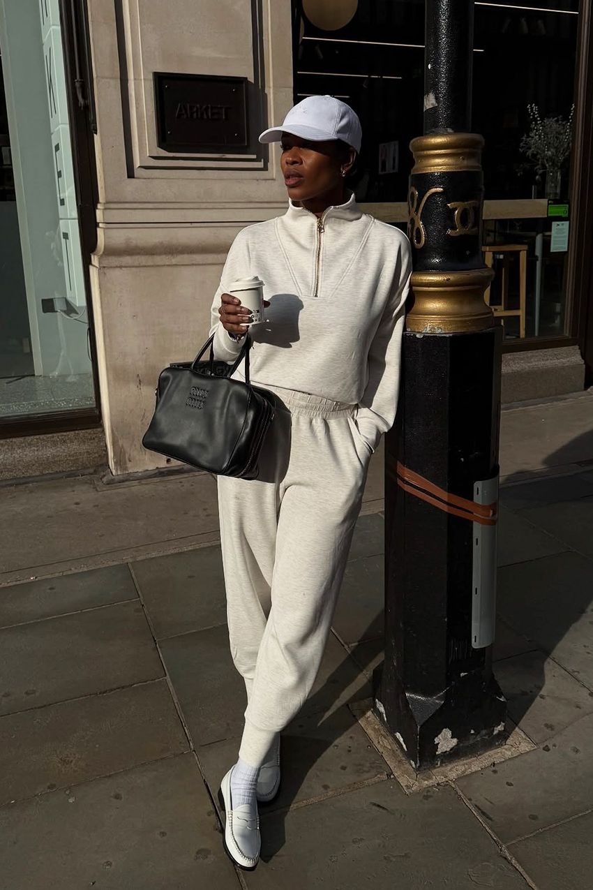 a woman wearing a white baseball bap with a quarter zip jacket and sweatpants
