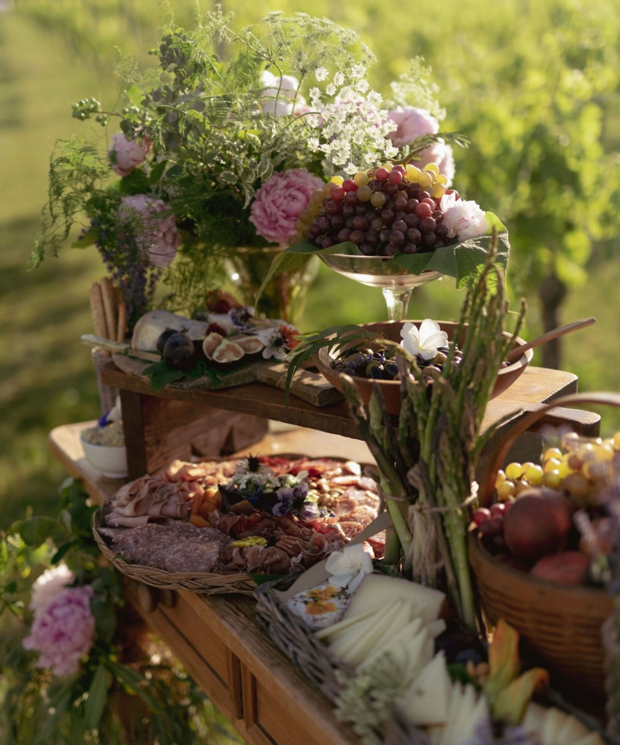 wooden table outdoors laden with plates of food ans vases of flowers