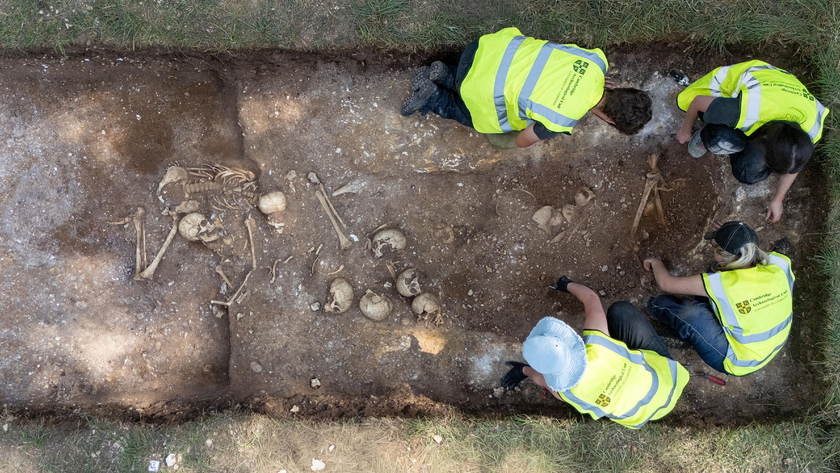 four people in blaze yellow vests excavate a trench full of human bones