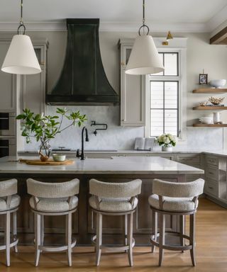 kitchen with gray kitchen island, gray bar stools, wooden floors, white pendants, marble workstops, tiled marble splashback,