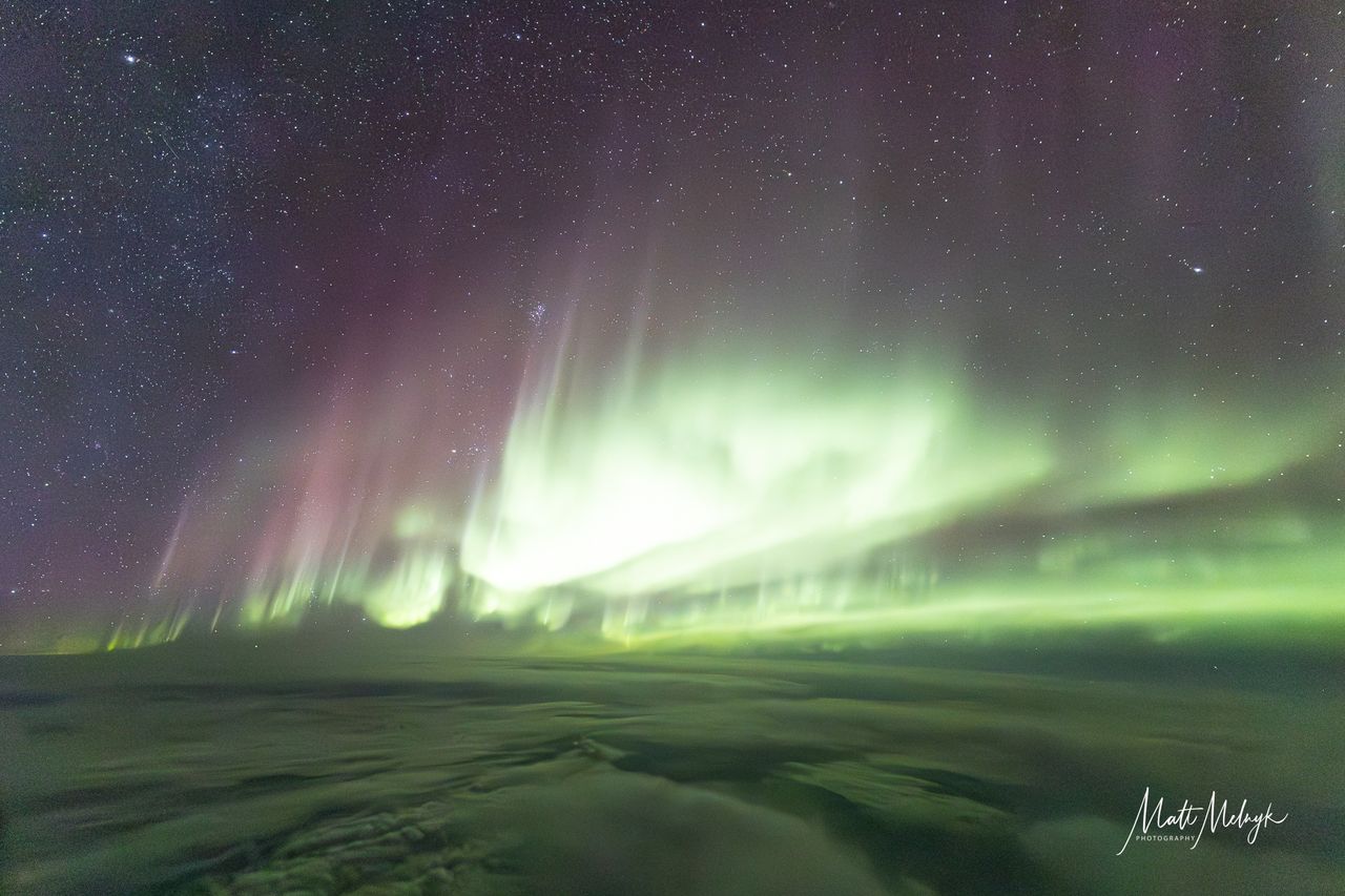 ribbons of green and purple light fill the sky in photos captured above the clouds from a dreamliner airplane.