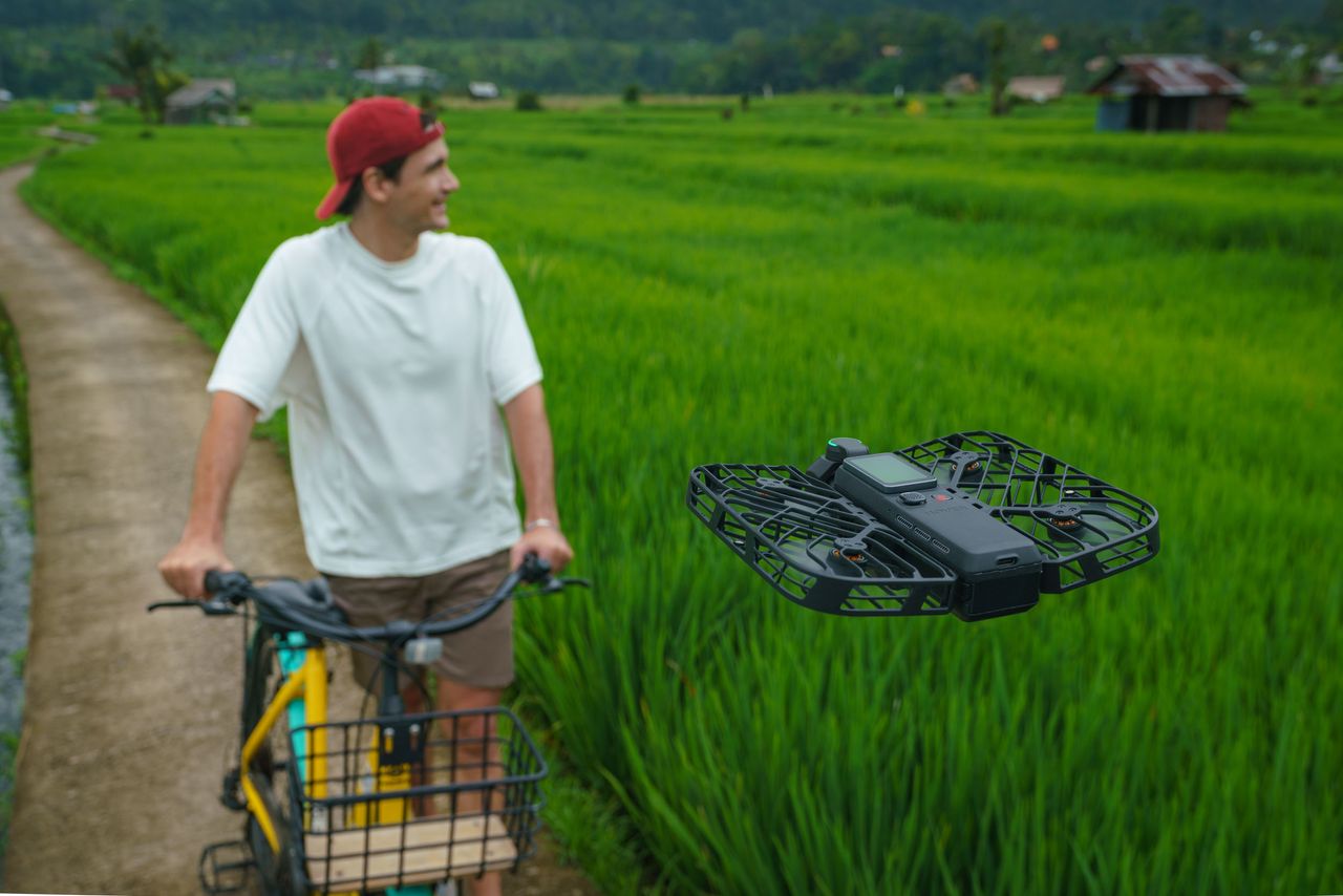 HoverAir Versa 2-in-1 drone and pocket gimbal camera in black, in flight tracking a man on a bike