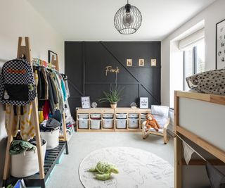 The bedroom of a young boy with black wall panelling and light carpet. There is a wooden clothes rail and a small armchair