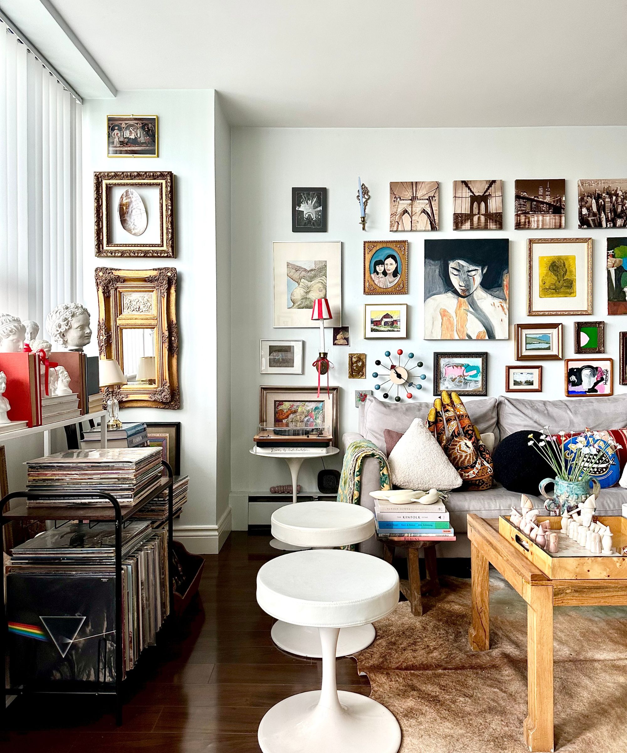 Living room with gallery wall with art and prints, wood coffee table, vinyls, sofa, and midcentury round stools