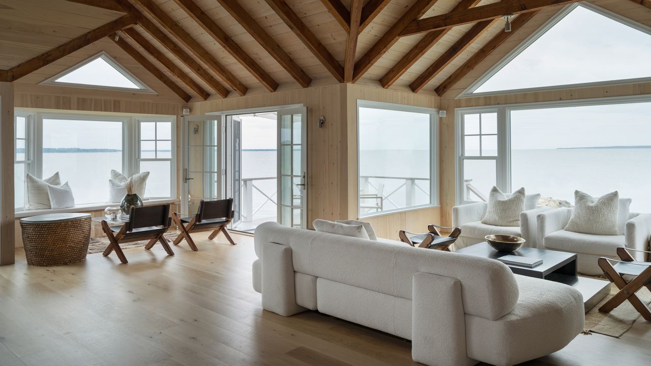 A living room with vaulted wooden ceilings, two seating areas, a white sofa and triangular-topped windows