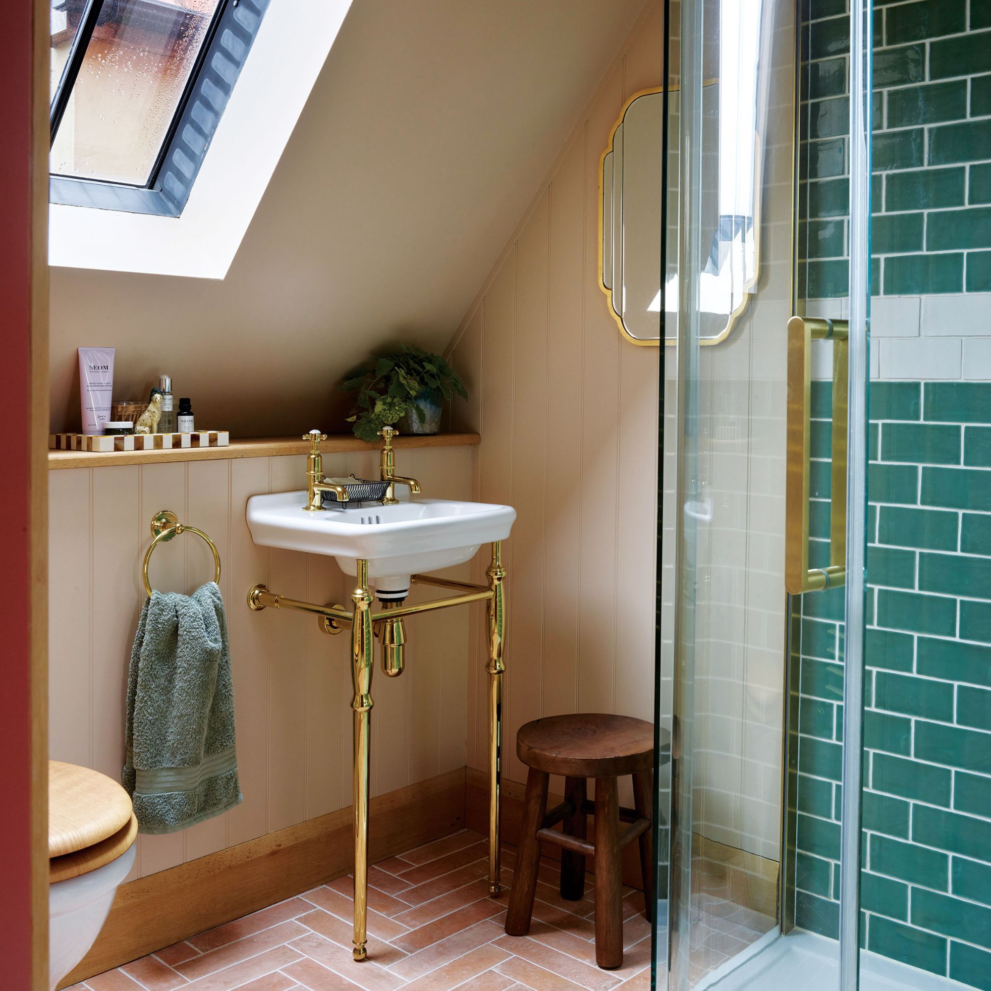 Colourful en-suite with gold accents, pink floor tiles, green shower tiles and wooden stool