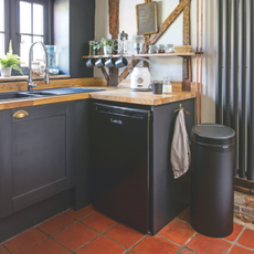 Black kitchen bin on red tiled floor, next to black kitchen cabinets.