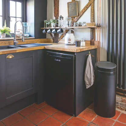 Black kitchen bin on red tiled floor, next to black kitchen cabinets.