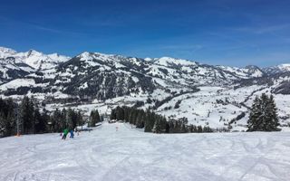 Skiing slope in the Gstaad winter sport area. In the background mountains and the village of Schonried. Gstaad, Switzerland.