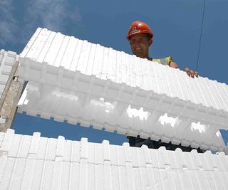 A BecoWallform 313 panel being installed by a man in a hard hat and hi-vis jacket on a building site. The ICF block is being lowered into place above other panels.