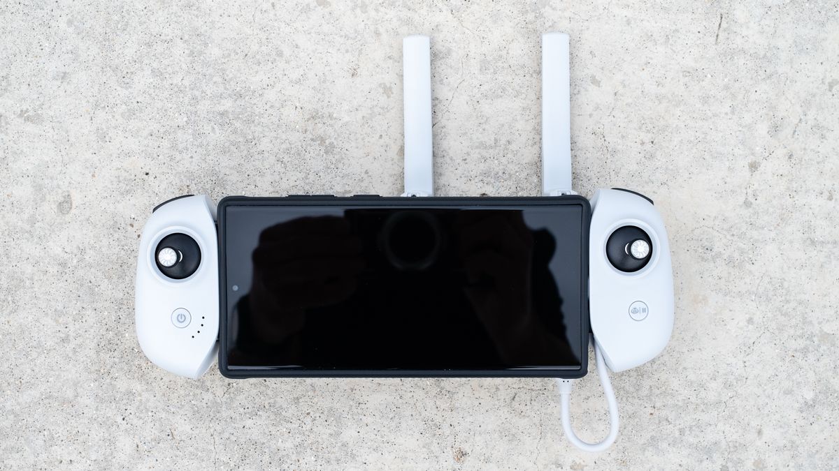 the top-down view of a white controller device, with two back joysticks on the left and right near the top of the grips. A black-screened device is held between the white grips, with two antennas sticking upward.