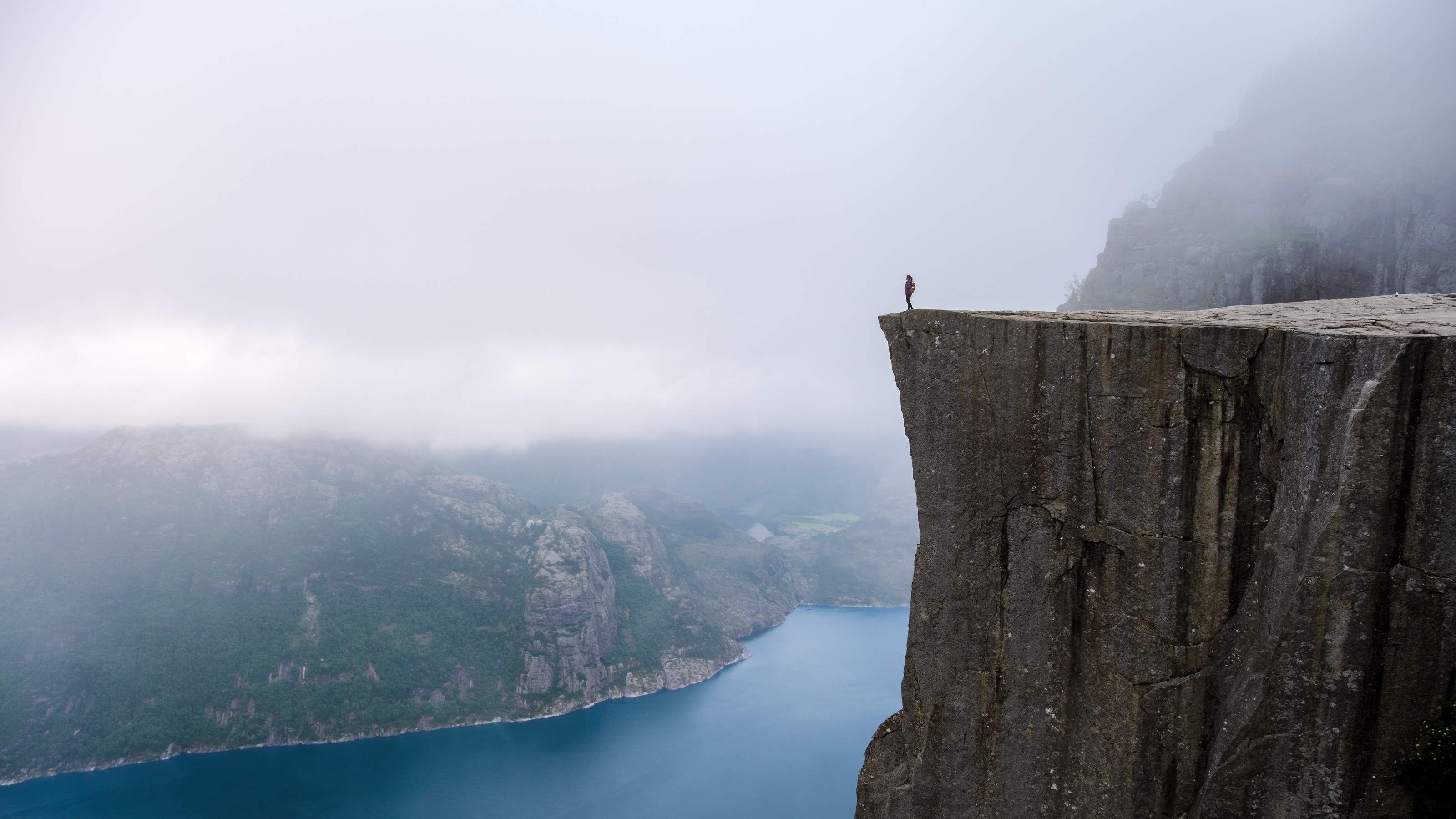 A distant view of a person standing near the edge of a very tall cliff.