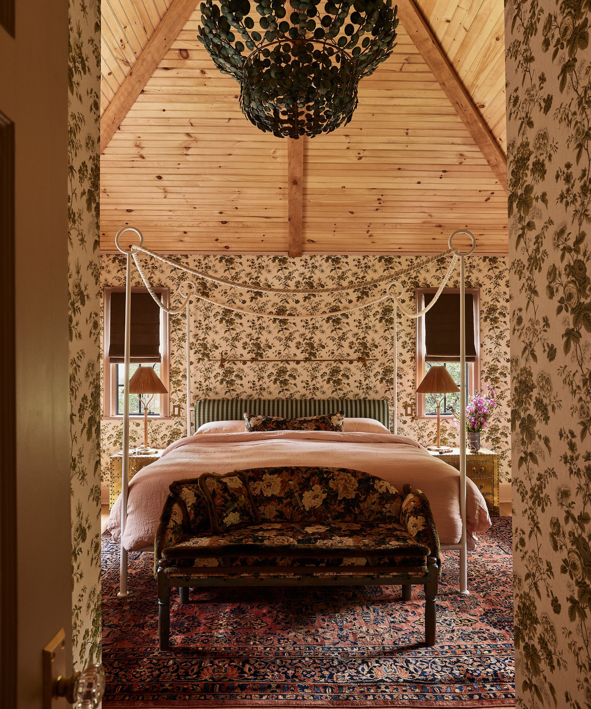 a white and brown floral bedroom with pine cathedral vaulted ceiling and a four poster bed with large chandelier overhead