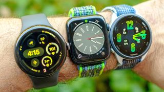 The Google Pixel Watch 3 in 45mm next to the Apple Watch SE 2022 and Garmin Forerunner 165 on a user&#039;s wrist with a green out of focus background