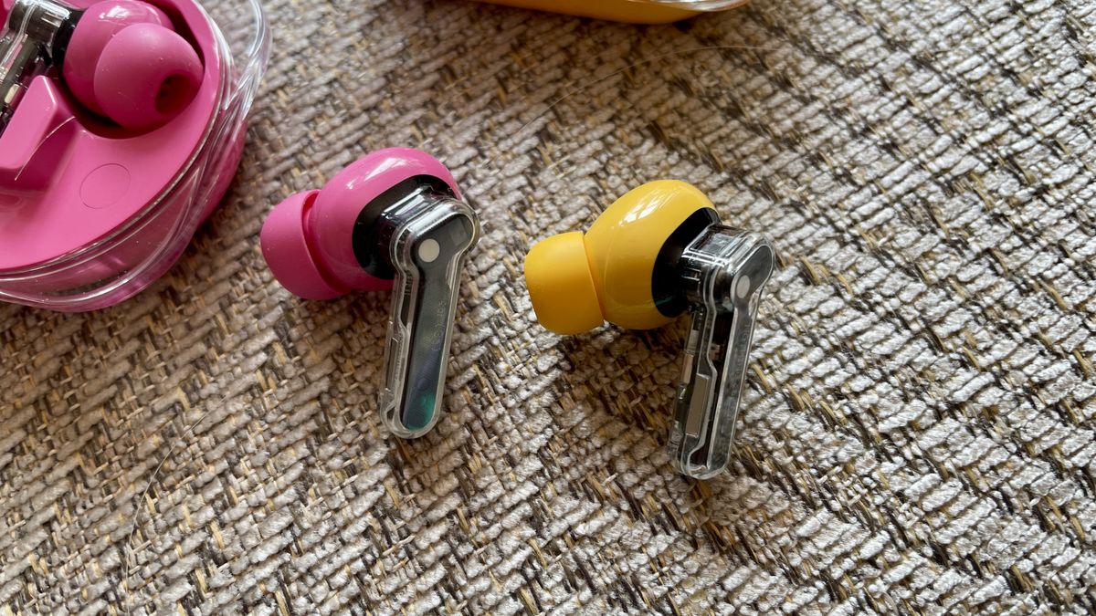 Nothing Ear (3a) in pink and Nothing Ear (a) in yellow, held in a hand and on beige background