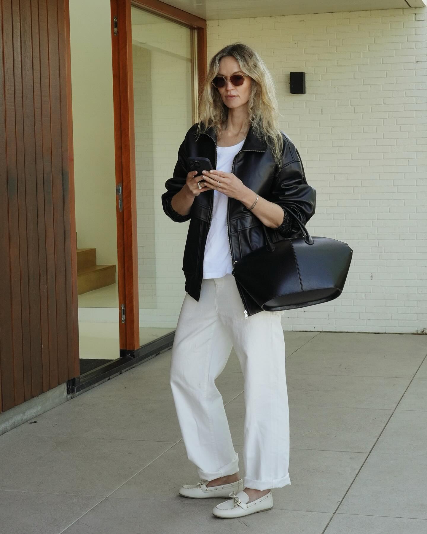 @anoukyve wears a pair of white boat shoes, white jeans and a leather jacket