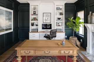 Home office with wooden desk, central white bookcase and dark painted wainscoting wall paneling