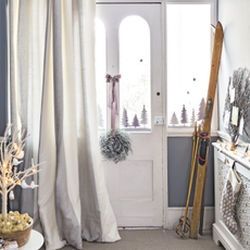 White period entrance hall front door, frosted wreath tiled with silver ribbon, draft excluder curtain, fir tree window decorations, vintage skis and poles