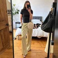 British style influencer Anna Newton poses for a mirror selfie in her London home wearing a black t-shirt, knotted bag, and pull-on satin pants