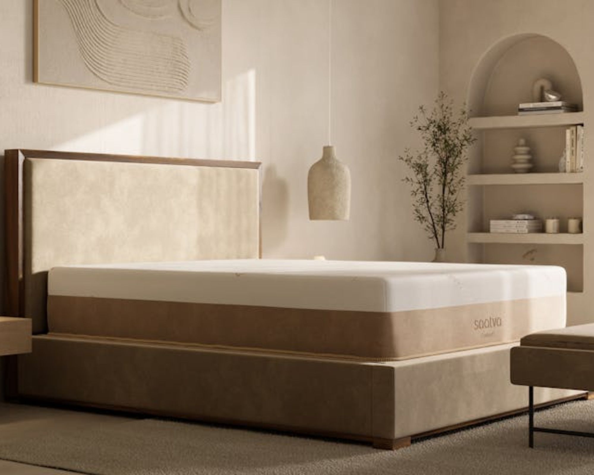 Saatva Contour5 on a neutral bedframe with neutral walls, artwork, a hanging lamp, and built-in arched shelving beside a small tree.