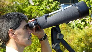 A man peers through a very large pair of binoculars mounted on a tripod.