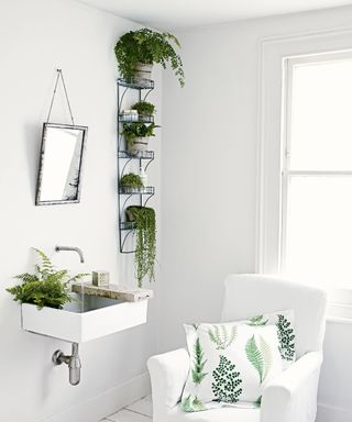 An example of bathroom shelf ideas showing a bathroom with white walls, a shelving unit filled with plants, and a white chair with a leaf-patterned cushion