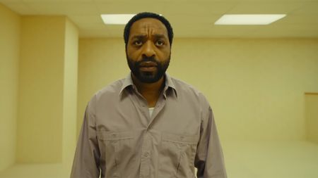Chiwetel Ejiofer wears a button down shirt and wanders around a seemingly abandoned office in Backrooms. 