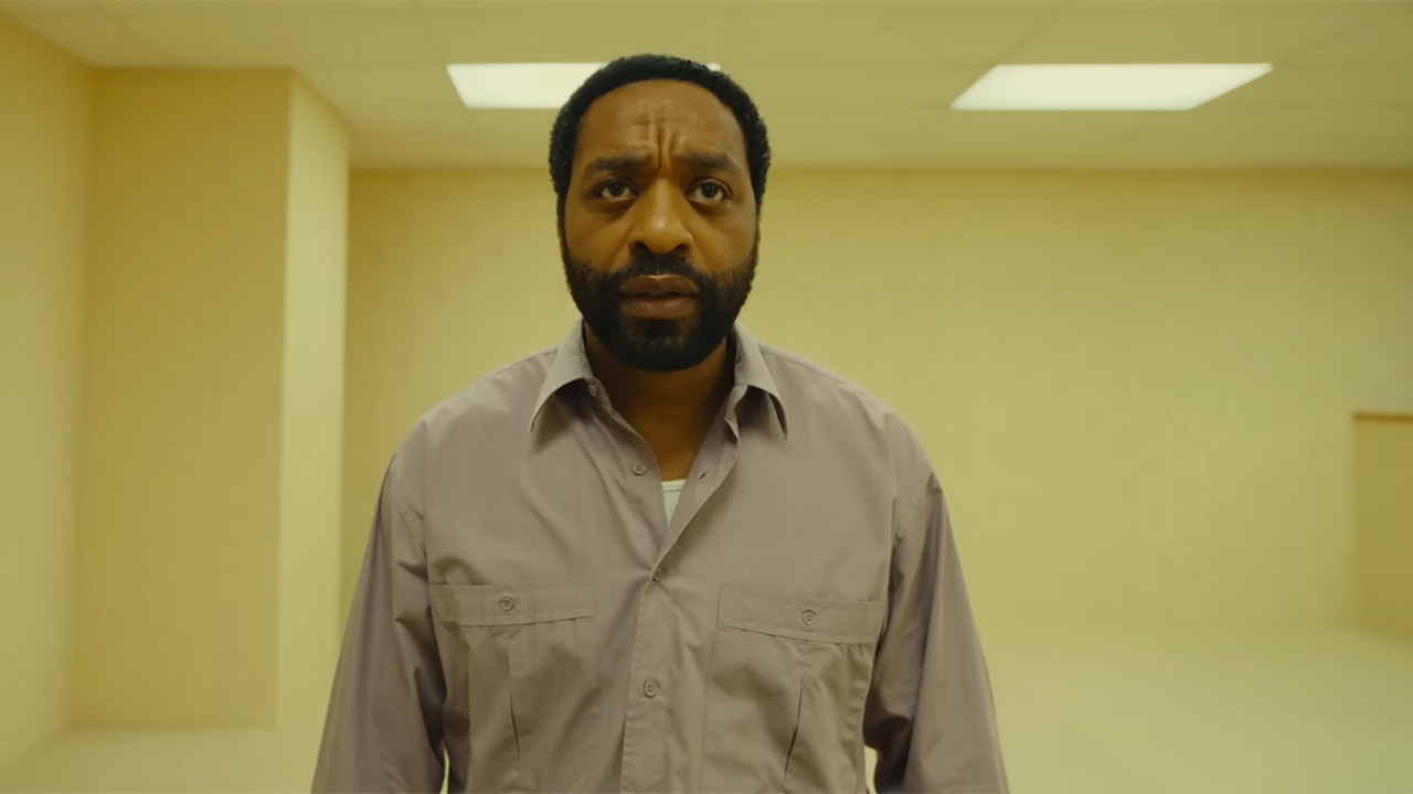 Chiwetel Ejiofer wears a button down shirt and wanders around a seemingly abandoned office in Backrooms. 