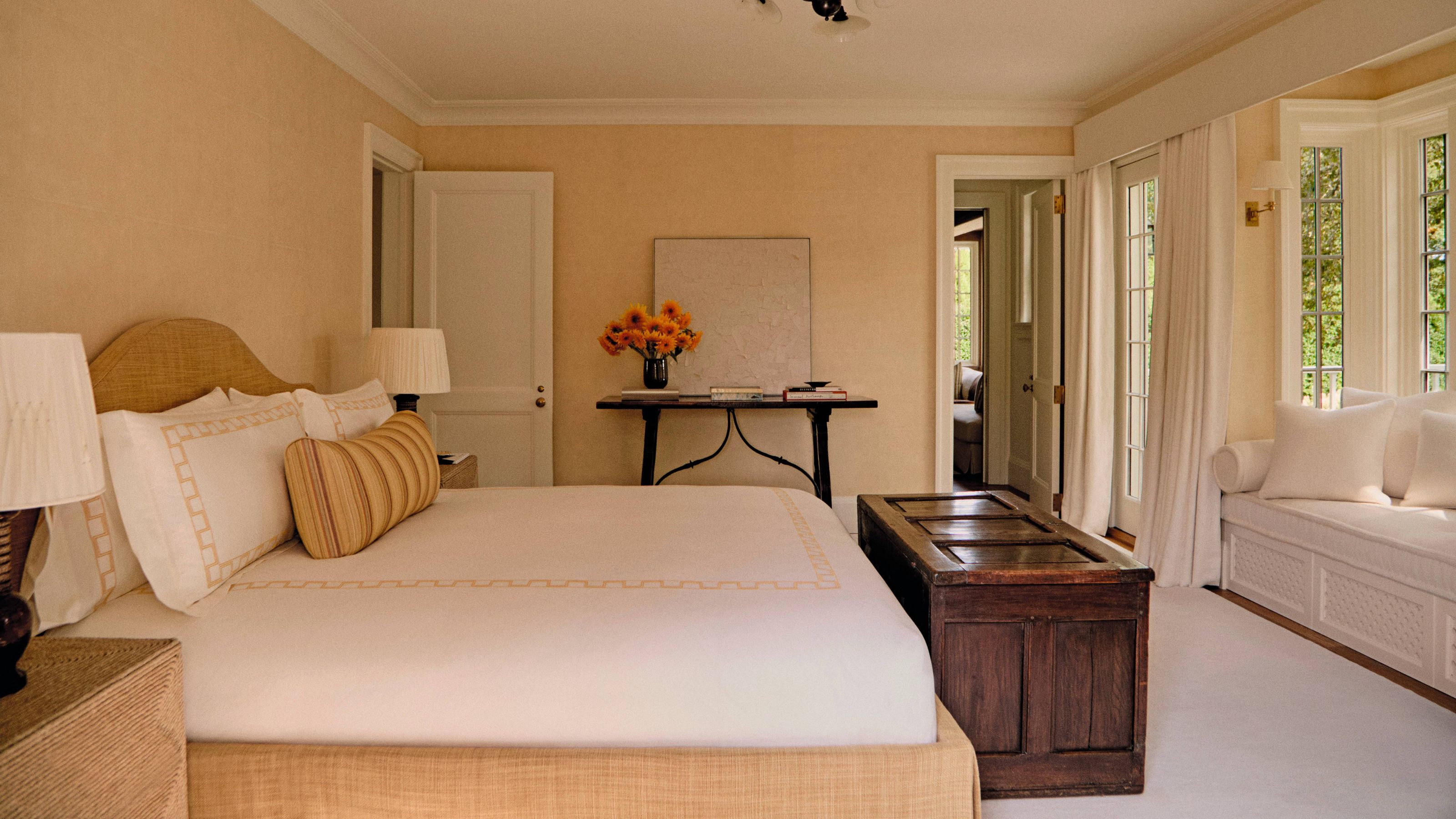 a textured butter yellow bedroom with yellow linen upholstered bed, antique wooden trunk and window nook