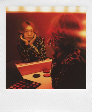 Polaroid photo of woman looking in mirror under red lighting