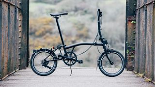 A black folding bike held up by a stick on an overpass