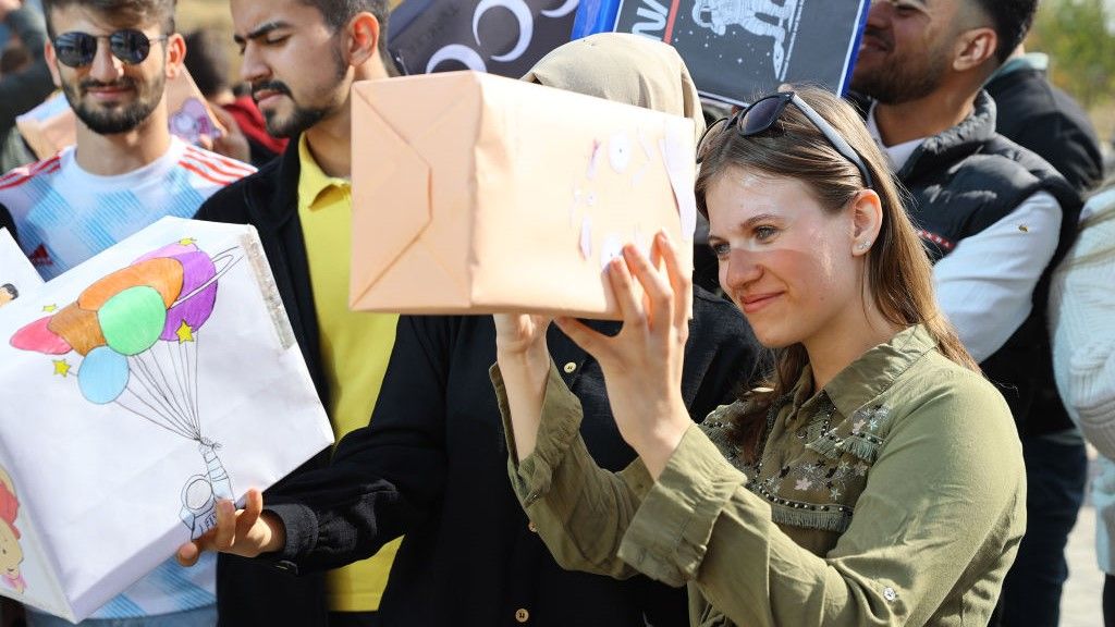 A woman looks through a solar eclipse viewer made from a shoe box
