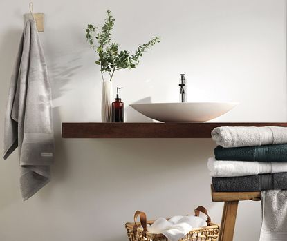 A wooden bathroom vanity with a vessel sink and a stack of towels on a wooden stool