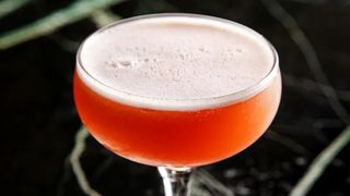 side shot of a coupe glass filled with red-orange liquid and a frothy top