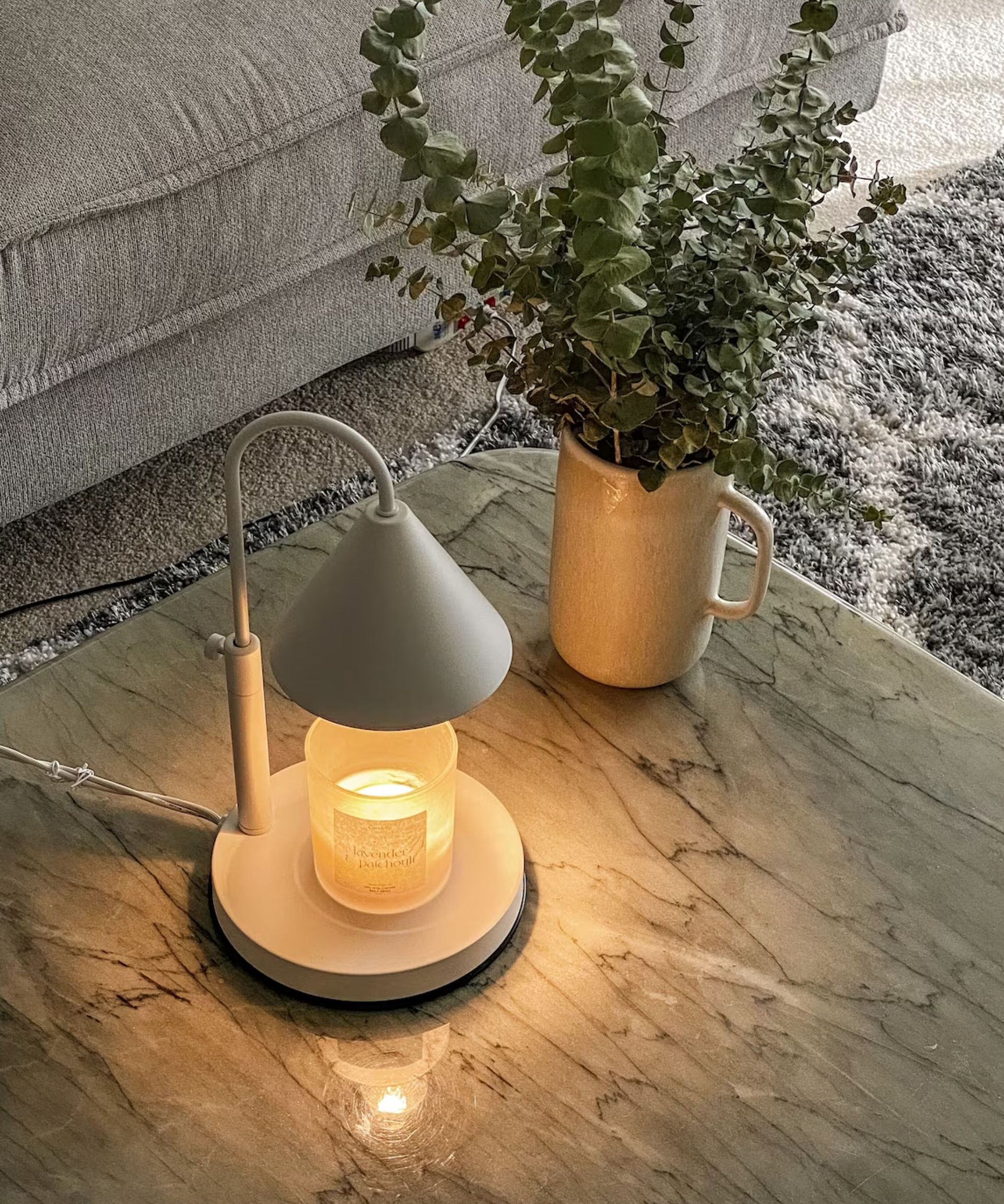 A white candle warming lamp turned on above a jar candle