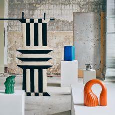 An industrial-style space filled with pillars displaying pieces from the IKEA KONSTRUNDA collection with a suspended black and white striped rug among them