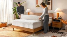 Best mattress toppers image shows a man and a woman unroll a Tempur-Adapt Mattress Topper onto their bed