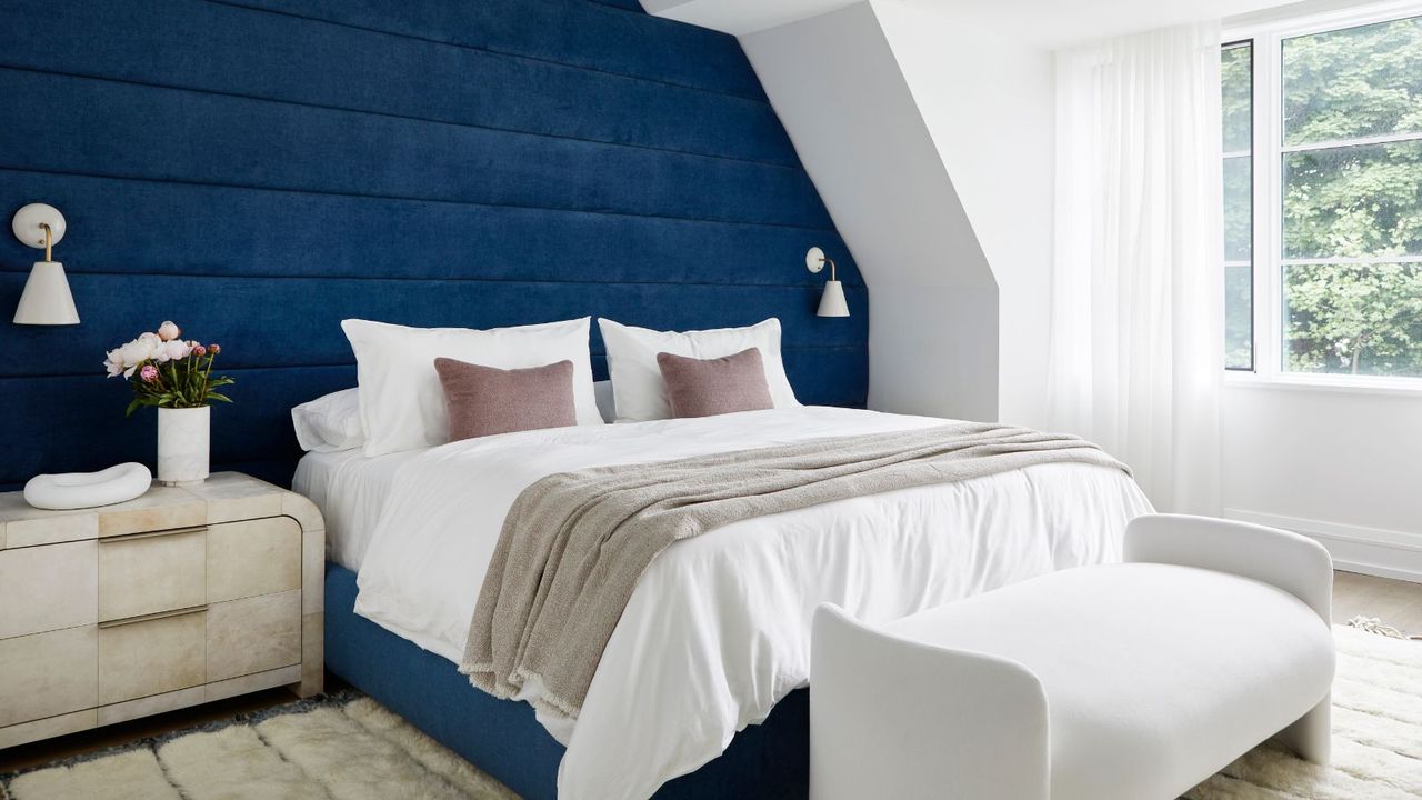 A bedroom by Ali Budd Interiors - a bed with white sheets against a blue wall.