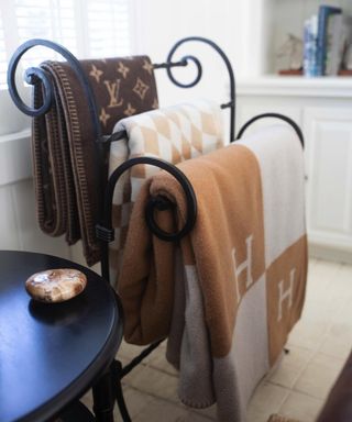 Scrolled metalwork blanket rack with three blankets hung on it next to round black table in living room