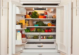 A fridge with the doors open and vegetables and milk inside