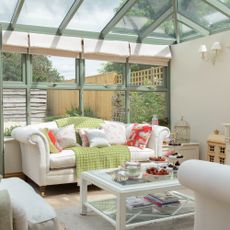 A conservatory with a living room set up with matching white sofas and an armchair